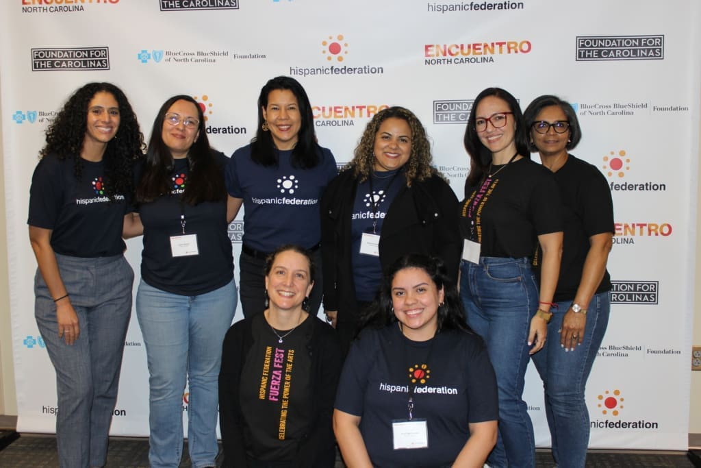 several women who work for Hispanic Federation posing for a photo behind an HF branded step and repeat